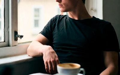 Молодой человек в чёрной футболке сидит у окна